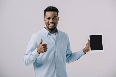 mutlu afrikalı amerikalı adam başparmak gösteren ve gri izole boş ekran ile dijital tablet tutarak 