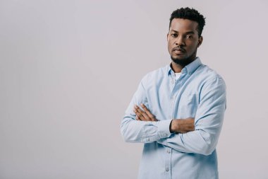 yakışıklı afro-amerikan adam kameraya bakıyor ve gri izole çapraz kolları ile ayakta 