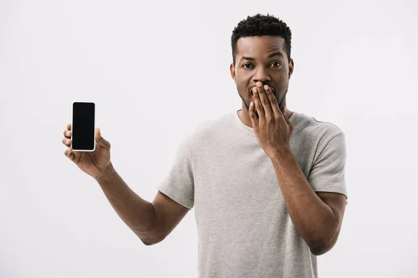 ショックを受けたアフリカ系アメリカ人男性が顔を覆い 白で隔離された空白の画面でスマートフォンを保持 — ストック写真