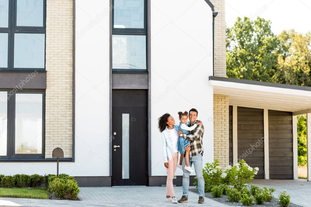 full length view of african american family standing near new house while father holding kid 