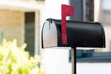 selective focus of black metal mailbox near green bushes before house clipart
