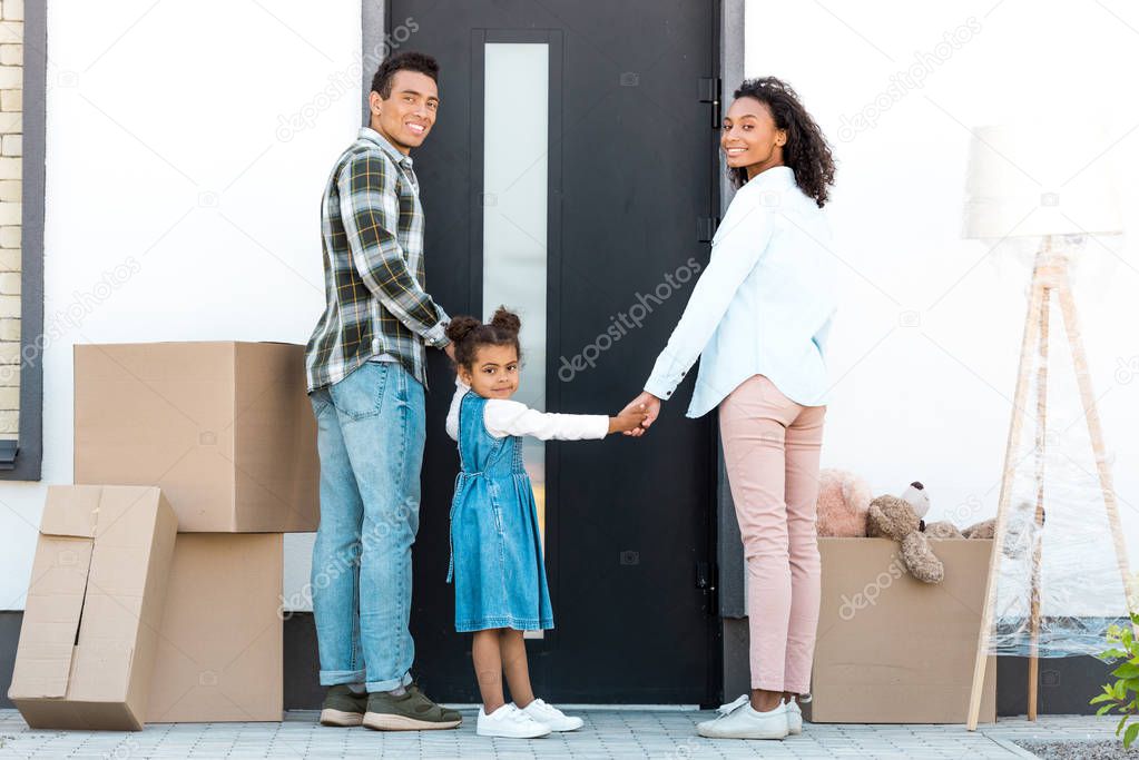 full length view of african american family looking at camera while standing in front of door of new house 