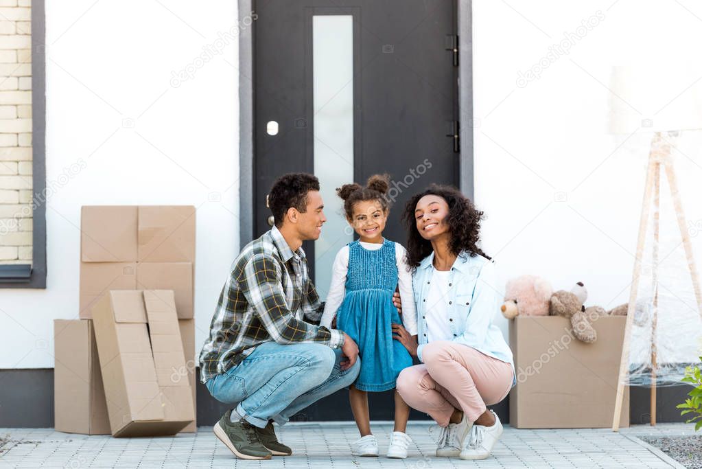 full length view of african american parent squatting near kid while mother and child looking at camera 