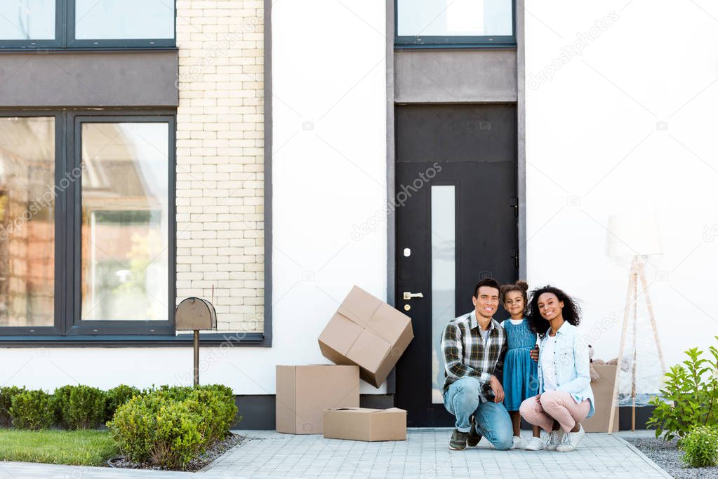 full length view of african american parent squatting near kid, smiling and looking at camera