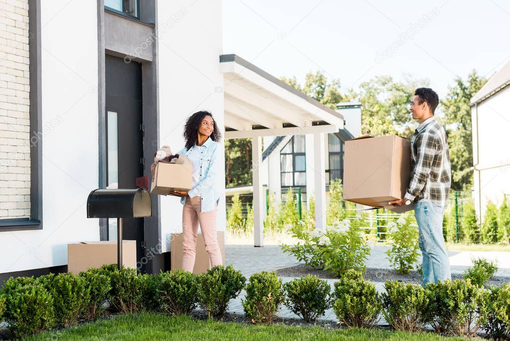 full length view of african american couple walking to house and holding boxes