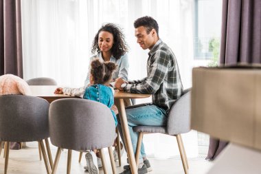 masanın önünde oturan, gülümseyen ve birbirine bakan Afrikalı-Amerikalı ailenin seçici odak 