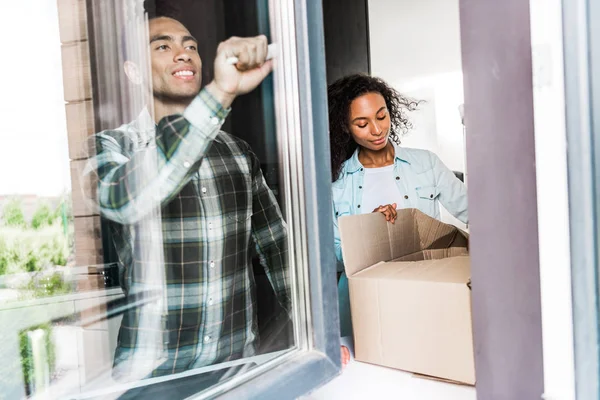 African American Husband Opening Window While Wife Opening Box — Stock Photo, Image