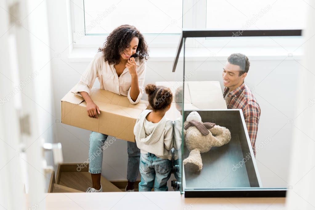 african american family going upstairs with boxes while kid looking at father