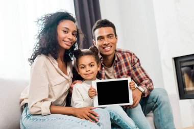 afro-amerikan ebeveynler gülümseyerek ve kameraya bakarken kamera dijital tablet gösteren çocuk 