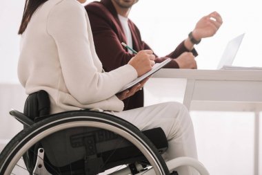 iş ortağı nın yanında otururken not defterine yazan engelli iş kadınının kırpılmış görünümü