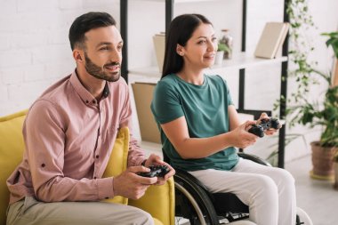 Kiev, Ukrayna - 10 Temmuz 2019: Evde video oyunu oynayan gülümseyen erkek arkadaşı ile neşeli engelli kadın.