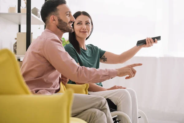 Cheerful Man Pointing Finger While Watching Together Disabled Girlfriend — Stock Photo, Image