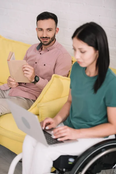 Attentive Disabled Woman Using Laptop Smiling Boyfriend Sitting Sofa Book — Stock Photo, Image