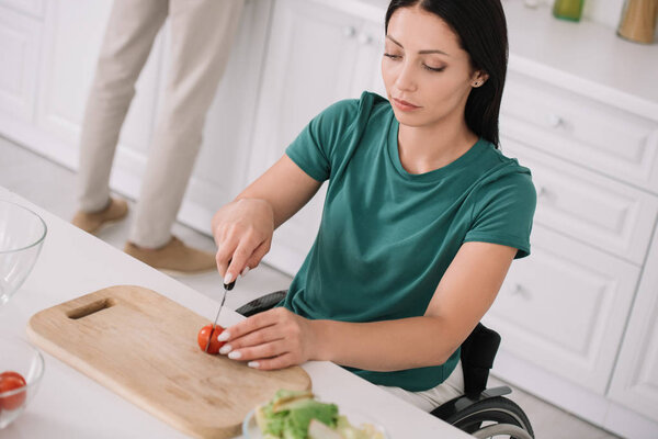 молодая женщина-инвалид режет помидоры на доске во время приготовления салата на кухне

