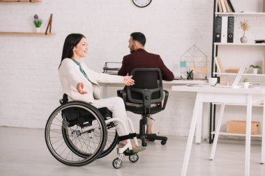 iş arkadaşı yanında tekerlekli sandalyede otururken neşeli engelli iş kadını gesturing