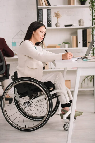 Attractive Disabled Businesswoman Writing Notebook While Sitting Wheelchair Workplace — Stock Photo, Image