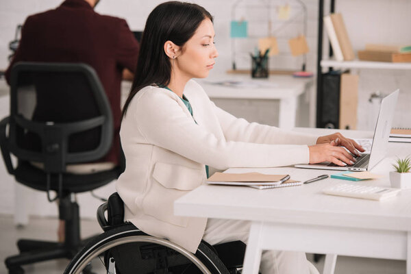 disabled businesswoman typing on laptop while sitting at workplace in offce