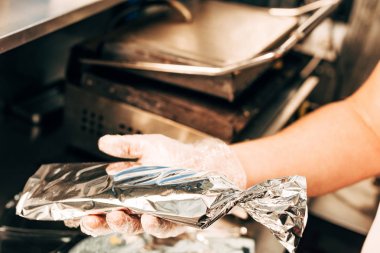 cropped view of cook in glove holding doner kebab in aluminium foil clipart