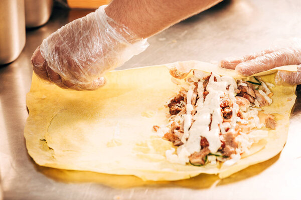 partial view of cook in gloves preparing doner kebab