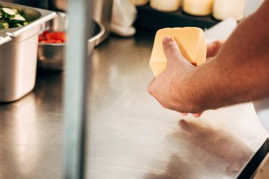 cropped view of cook holding cheese at workplace clipart