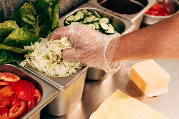 partial view of cook in glove holding cut lettuce at workplace