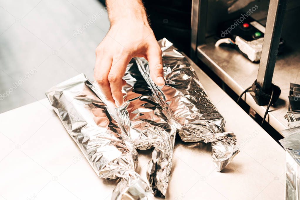 cropped view of man and doner kebabs in aluminium foil