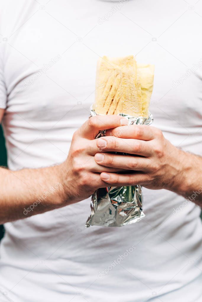 partial view of man holding doner kebab in aluminium foil