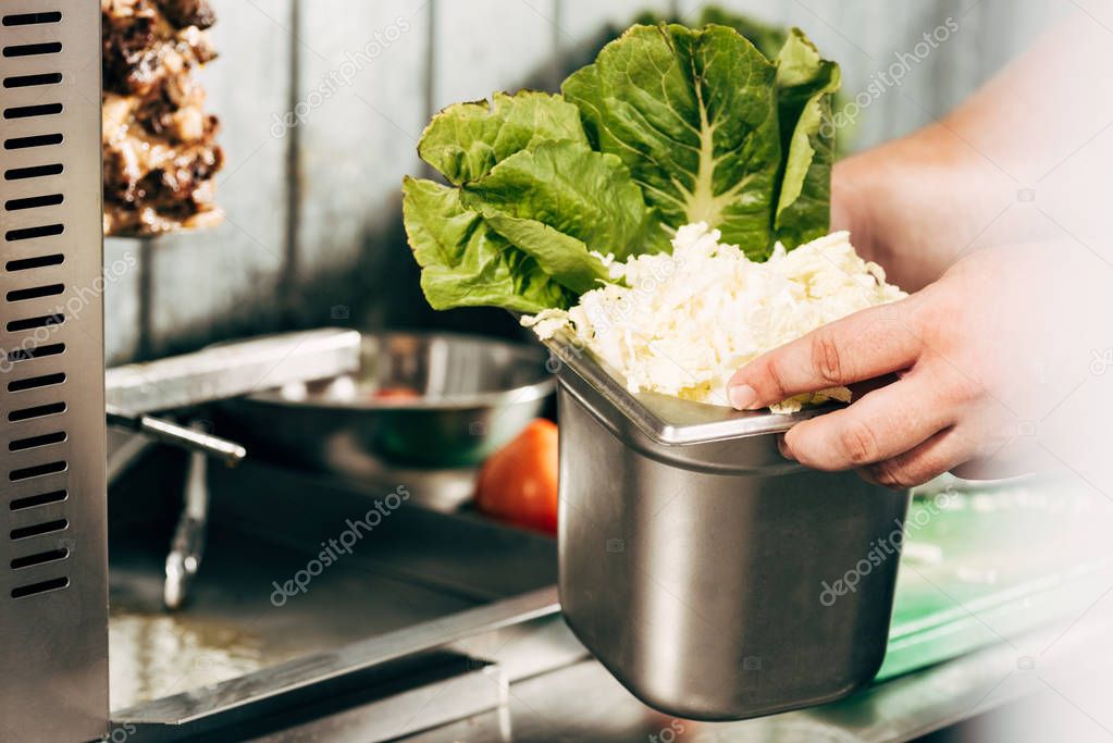 cropped view of cook holding container with cut lettuce 