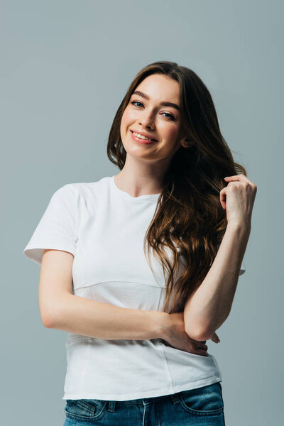 happy beautiful girl in white t-shirt touching hair isolated on grey