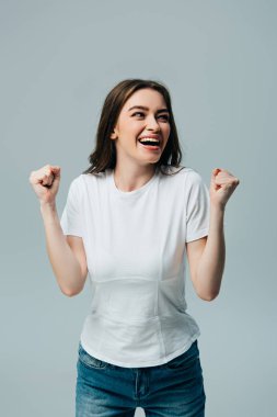 happy beautiful girl in white t-shirt showing yes gesture and looking away isolated on grey clipart