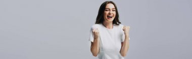 shocked happy beautiful girl in white t-shirt touching face isolated on grey clipart