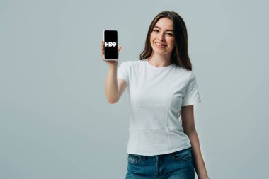 Kiev, Ukrayna - 6 Haziran 2019: gri üzerinde izole Hbo uygulaması ile akıllı telefon gösteren beyaz t-shirt mutlu güzel kız