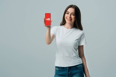 Kiev, Ukrayna - 6 Haziran 2019: gri izole youtube uygulaması ile akıllı telefon gösteren beyaz t-shirt mutlu güzel kız