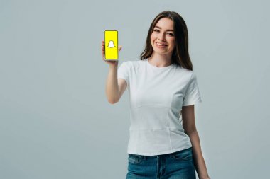 Kiev, Ukrayna - 6 Haziran 2019: gri üzerinde izole snapchat uygulaması ile akıllı telefon gösteren beyaz t-shirt mutlu güzel kız