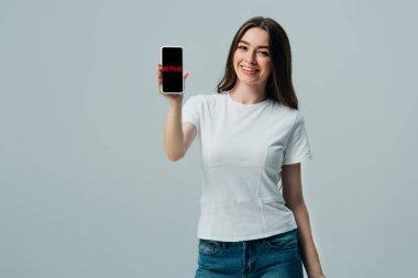 Kiev, Ukrayna - 6 Haziran 2019: Gri üzerinde izole Netflix uygulaması ile akıllı telefon gösteren beyaz t-shirt mutlu güzel kız