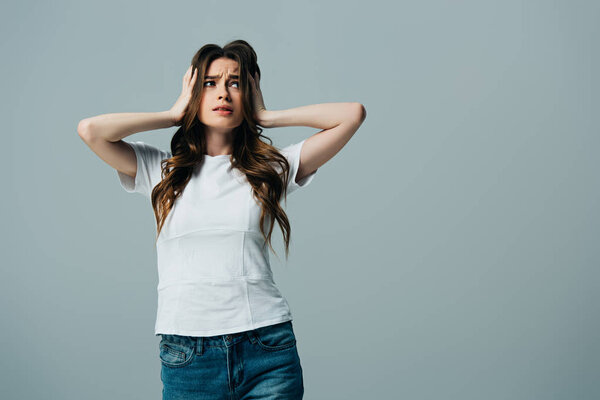 уставшая красивая девушка в белой футболке касаясь головы, изолированной от серого
