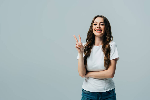 happy beautiful girl in white t-shirt showing victory sign isolated on grey