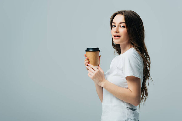 side view of smiling beautiful girl in white t-shirt with paper cup isolated on grey