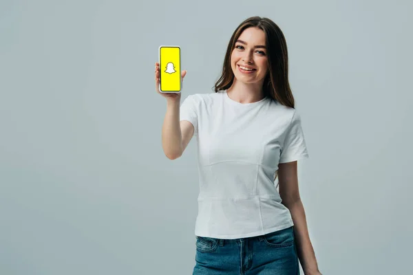乌克兰 2019年6月6日 快乐美丽的女孩在白色T恤显示智能手机与Snapchat应用程序隔离在灰色 — 图库照片