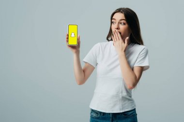 Kiev, Ukrayna - 6 Haziran 2019: gri üzerinde izole Snapchat uygulaması ile akıllı telefon gösteren beyaz t-shirt şok güzel kız
