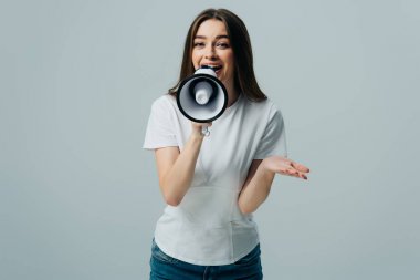 young pretty woman speaking in megaphone isolated on grey clipart