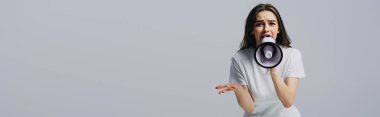 young pretty woman screaming in loudspeaker isolated on grey, panoramic shot clipart