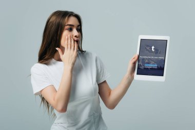 Kiev, Ukrayna - 6 Haziran 2019: Gri üzerinde izole Tumblr uygulaması ile dijital tablet gösteren beyaz t-shirt güzel kız şok