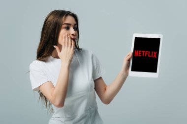 Kiev, Ukrayna - 6 Haziran 2019: Gri üzerinde izole Netflix uygulaması ile dijital tablet gösteren beyaz t-shirt güzel kız şok