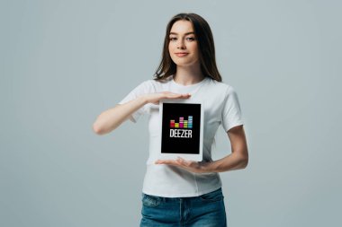 Kiev, Ukrayna - 6 Haziran 2019: gri izole deezer uygulaması ile dijital tablet gösteren beyaz t-shirt gülümseyen güzel kız