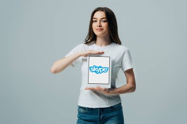 Kiev, Ukrayna - 6 Haziran 2019: gri üzerinde izole Skype uygulaması ile dijital tablet gösteren beyaz t-shirt gülümseyen güzel kız