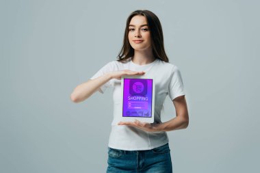 gri izole online alışveriş uygulaması ile dijital tablet gösteren beyaz t-shirt gülümseyen güzel kız