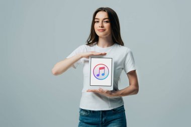 Kiev, Ukrayna - 6 Haziran 2019: beyaz tişörtlü gülümseyen güzel kız, gri üzerinde izole edilmiş apple müzik uygulaması ile dijital tablet ilerler