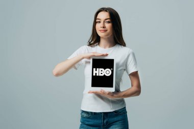 Kiev, Ukrayna - 6 Haziran 2019: gri üzerinde izole Hbo uygulaması ile dijital tablet gösteren beyaz t-shirt gülümseyen güzel kız