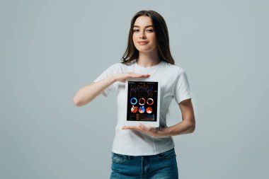 gri izole finansal uygulama ile dijital tablet gösteren beyaz t-shirt gülümseyen güzel kız